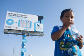 A Child Drinks Water Infront of a Water Generating Billboard